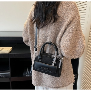 Détail d'un sac Boston noir chic avec nœud en cuir et ruban à carreaux sur la sangle