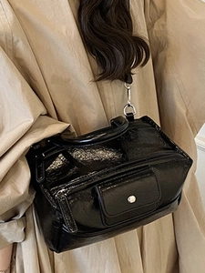 Glossy black patent leather Boston handbag with silver hardware shown on a trench coat