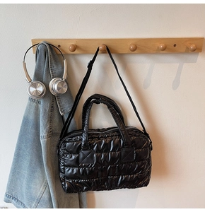 Détail d'un sac cabas noir matelassé suspendu à un crochet en bois, style minimaliste