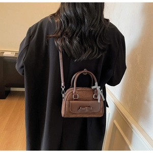 Détail du sac Boston en velours marron avec nœud et foulard à carreaux sur modèle