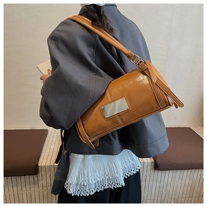 Chic brown leather cylinder shoulder bag with silver metal plaque on model