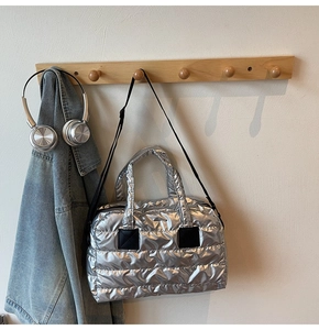 Détail d'un sac cabas argenté matelassé suspendu à un crochet avec des écouteurs en décor