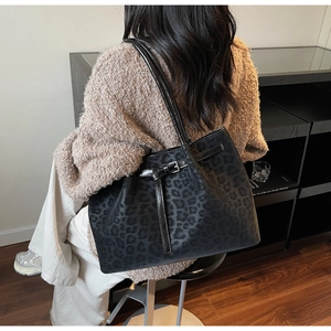Detail view of black leopard print tote bag worn on shoulder by a model in a cozy room