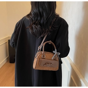 Gros plan d'un mini sac Boston marron en daim avec nœuds porté par un mannequin