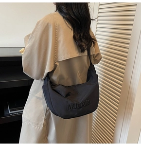 Detail of a chic black hobo bag with embossed lettering on a stylish beige trench coat