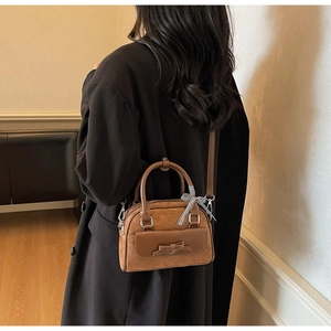 Détail du sac à main en daim marron avec nœud en cuir et ruban à carreaux sur modèle