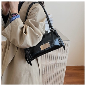 Detail of high-gloss black patent leather baguette bag with silver metal plate accent