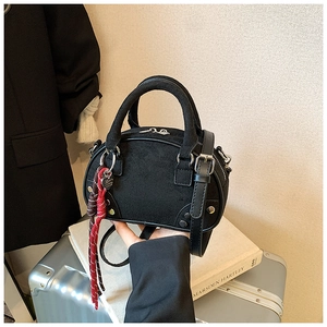 Detail of a black bowling handbag featuring a woven charm and dual handles