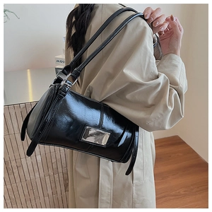 Detail shot of a black glossy cylinder bag with silver hardware and sleek shoulder straps