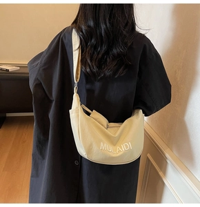 Close-up of cream canvas half-moon crossbody bag with 3D MULAIDI lettering on black coat