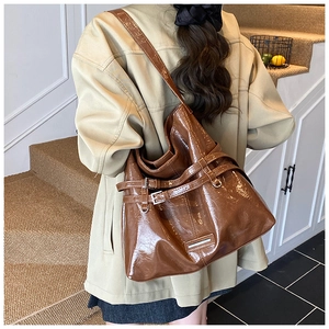 Brown glossy leather tote bag with buckle details shown on a model in a warm indoor setting