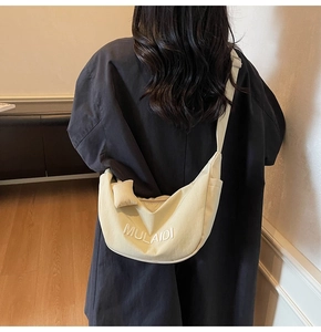 Detail of cream canvas crescent crossbody bag with MULAIDI embroidery and adjustable strap