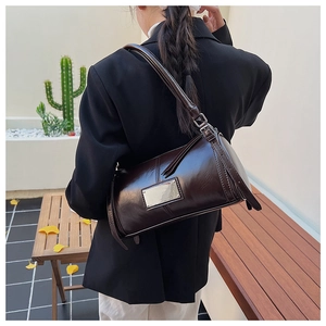 Detail view of a vintage dark brown cylindrical shoulder bag worn by a model in a garden