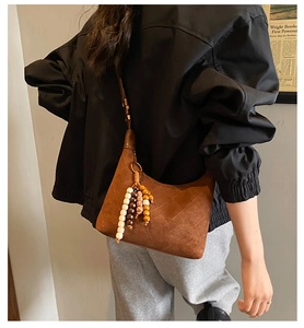 Detail of brown suede crossbody bag featuring diamond quilting and beaded tassel accent