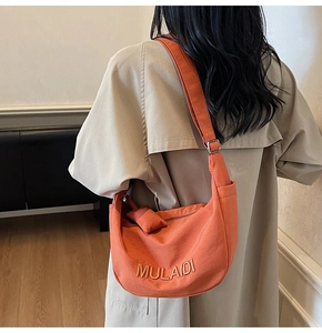 Detail of an orange canvas half-moon crossbody bag with MULAIDI embroidery and silver buckle