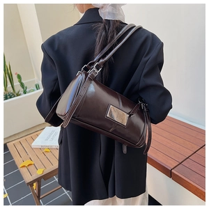 Outdoor shot showing the glossy dark brown shoulder bag with silver metal plaque detail