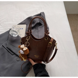 Detailansicht der dunkelbraunen PU-Handtasche mit Bronzebeschlägen und Plüschbär-Anhänger