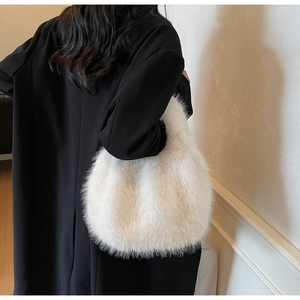 Détail d'un sac à bandoulière en fausse fourrure blanche porté avec un long manteau noir