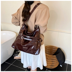 Deep brown glossy leather tote bag with decorative buckle and wide strap on model