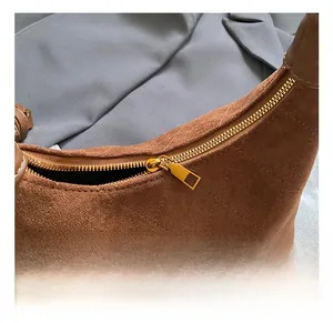 Detailed close-up of premium golden metal zipper and brown suede texture on shoulder bag