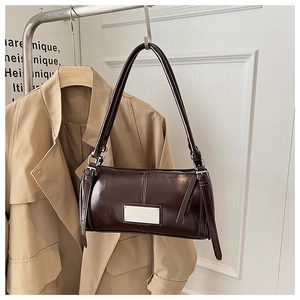 Detailed macro view of dark brown patent leather shoulder bag with silver hardware plate