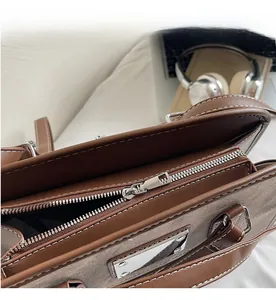 Detail of smooth silver zipper and stitching on a brown leather and grey fabric bag