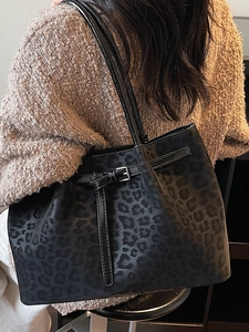 Chic black leopard embossed tote bag worn by a person in a cozy minimalist sweater