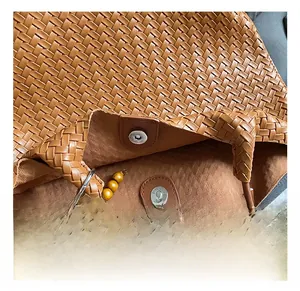 Detail of brown woven leather tote with magnetic closure and decorative beaded charm