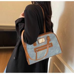 Detail of gray-blue shoulder bag with brown leather trim and metallic zipper plaque