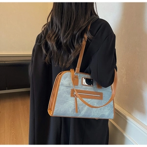 Detail of light blue denim textured shoulder bag with brown leather straps on a model