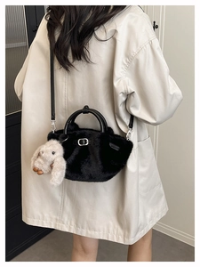 Détail d'un sac seau en peluche noire avec breloque lapin sur un manteau beige