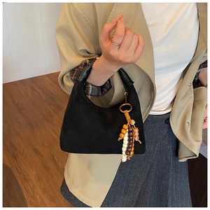 Detail of black quilted suede handbag featuring a curved handle and colorful beaded tassel