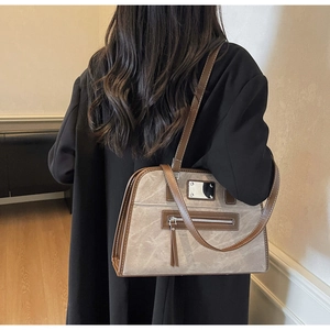 Detail of grey vintage tote bag with brown leather trim and metallic accents on black coat