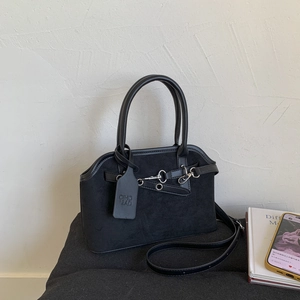 Detail of black suede handbag with metal buckle and branded leather hangtag on handle