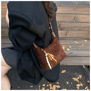 Detail of dark brown suede crescent shoulder bag with quilted texture and beaded tassel