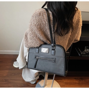 Detail showing the black tote bag with white contrast stitching and silver brand plaque