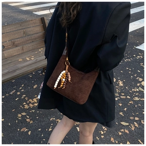 Close-up of brown suede shoulder bag with diamond stitching and beaded tassel detail