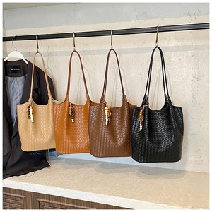 Detail of four handmade woven tote bags in beige, brown, and black with wooden beads
