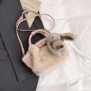 Détail du sac seau en peluche rose avec pendentif lapin sur un fond de tissu texturé