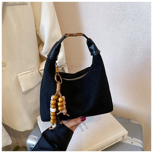Detail of black quilted shoulder bag featuring wooden bead tassels and gold metal hardware