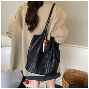 Detail of hand-woven black leather tote bag with wooden bead charm on shoulder strap