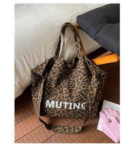 Detail showing the leopard print canvas tote bag with white MUTING lettering on a wood floor
