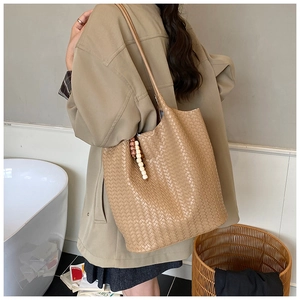 Detail of hand-woven khaki tote bag with beaded charm detail on a model shoulder