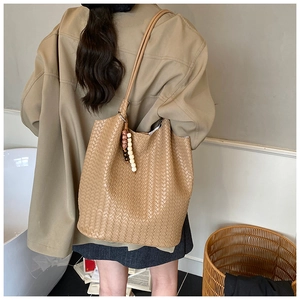 Detail of tan woven tote bag with bohemian bead tassel charm and long shoulder strap