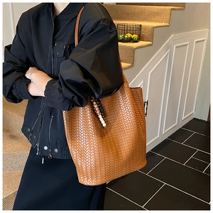 Detail view of brown woven tote bag with beaded tassel charm on a model shoulder