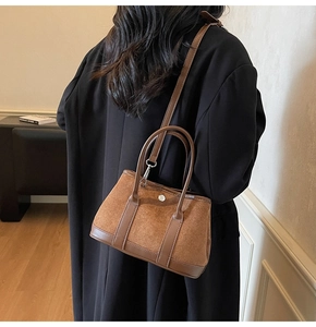 Detail view of brown suede and leather bucket bag featuring silver buckle and dual handles