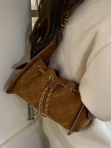 Brown quilted suede shoulder bag with gold chain strap shown on a female model