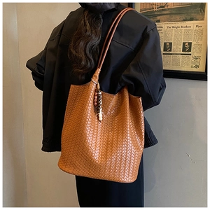 Close-up of brown woven leather tote bag featuring detailed texture and bohemian wood bead charm