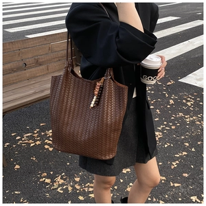 Close-up of woven dark brown leather tote with ethnic beaded charm and long straps