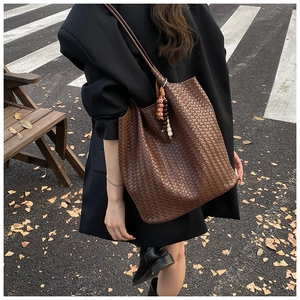 Close-up of brown woven leather tote bag with ethnic wooden beads in outdoor urban setting